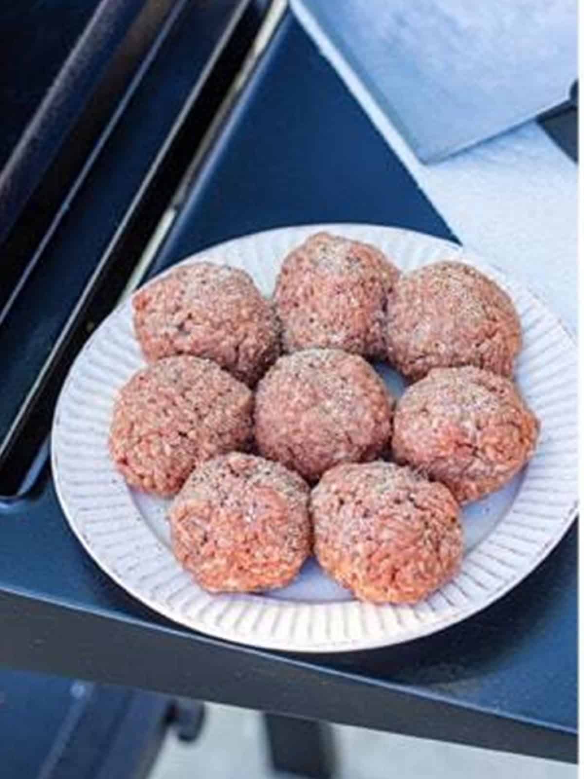 Ground beef portioned and rolled into loose balls on a plate for smash burgers.