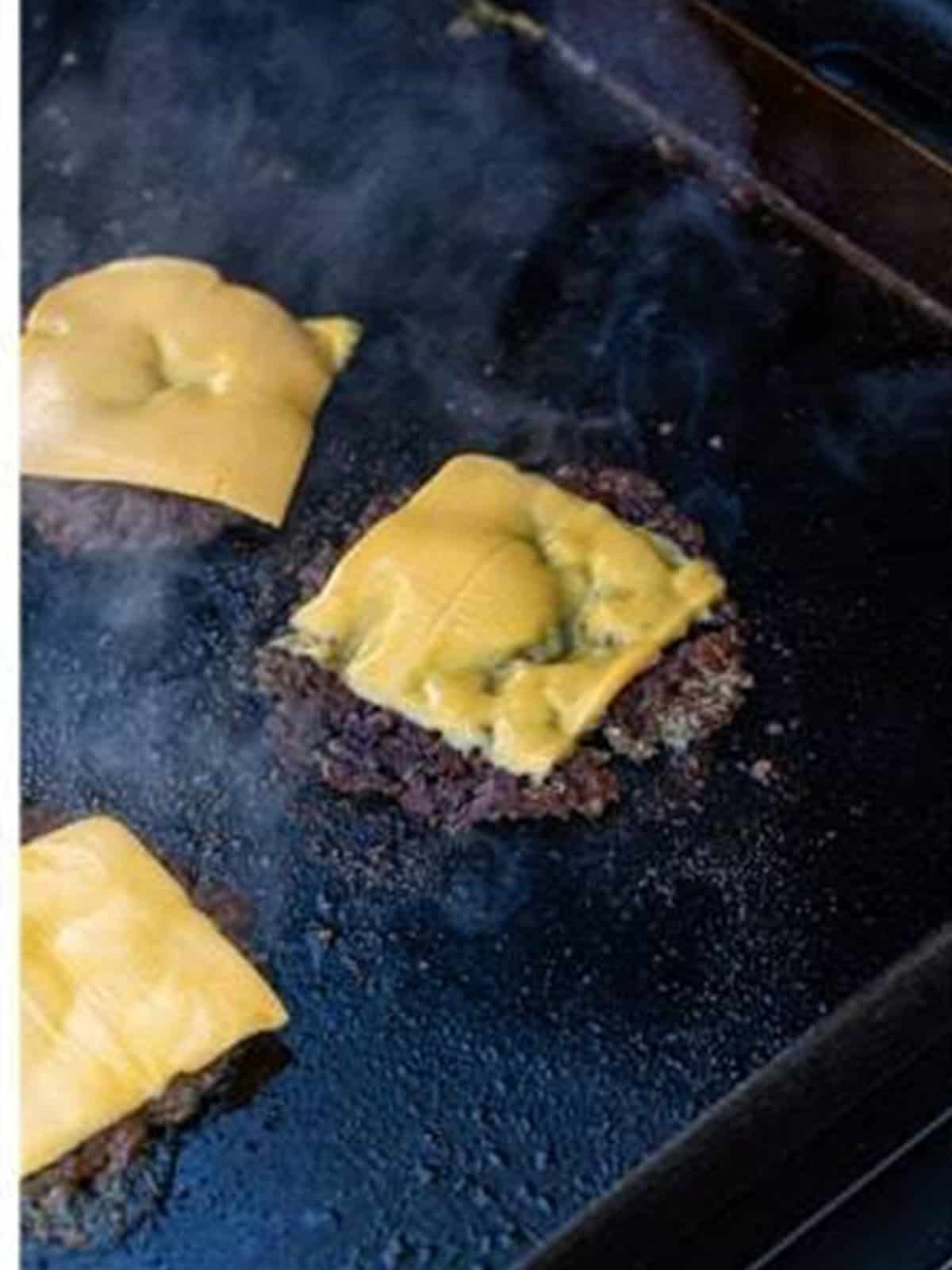 American cheese melting on a flipped smash burger patty on the griddle.
