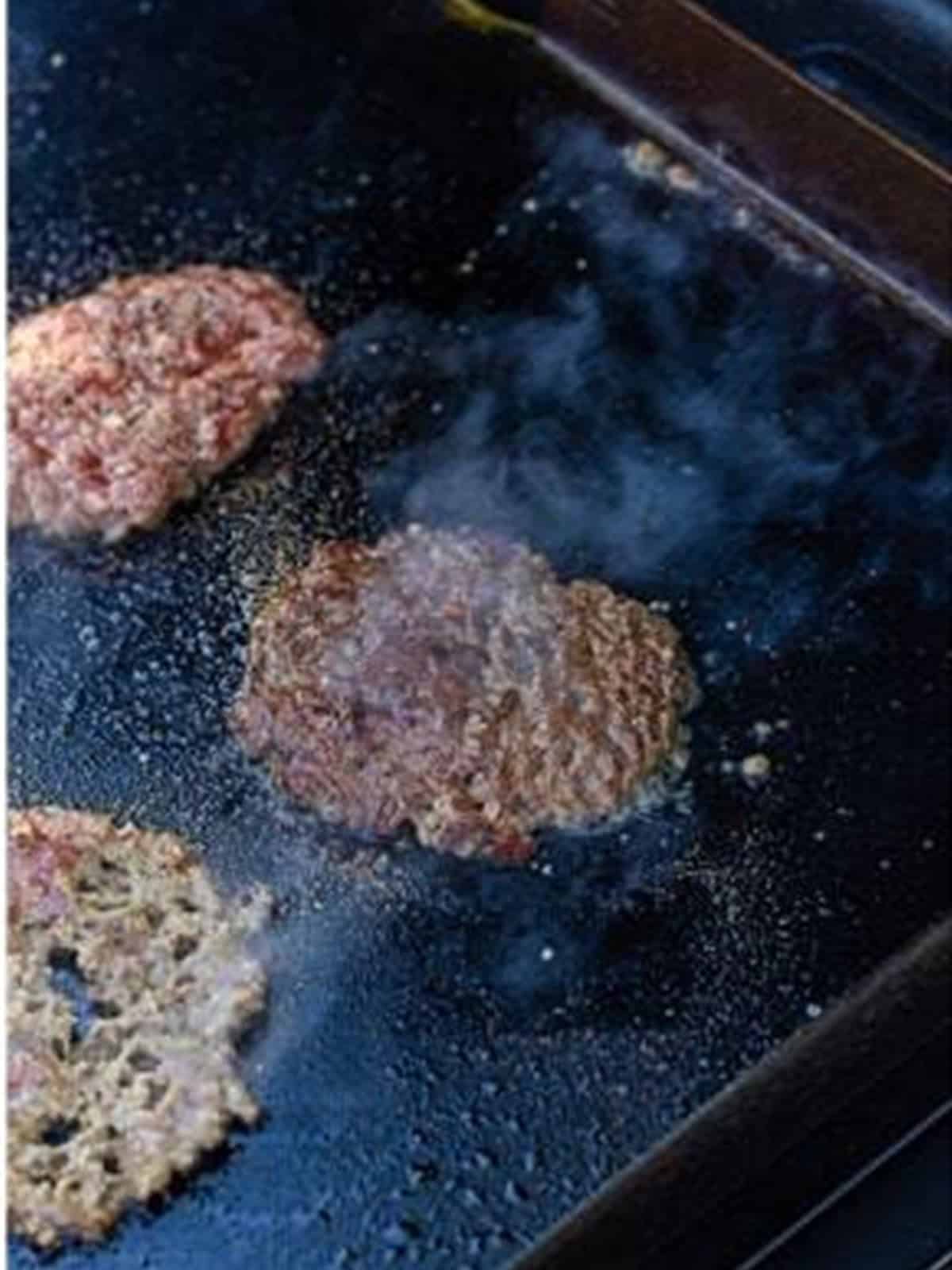 A smash burger patty cooking until lacy and browned around the edges.