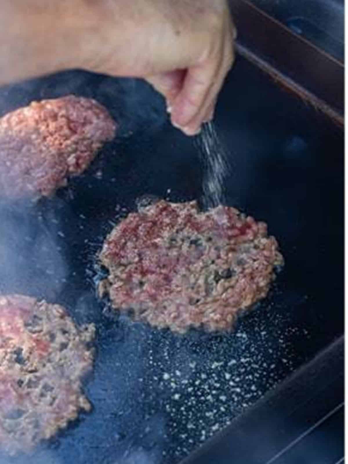Seasoning sprinkled over a smashed beef patty on the griddle.