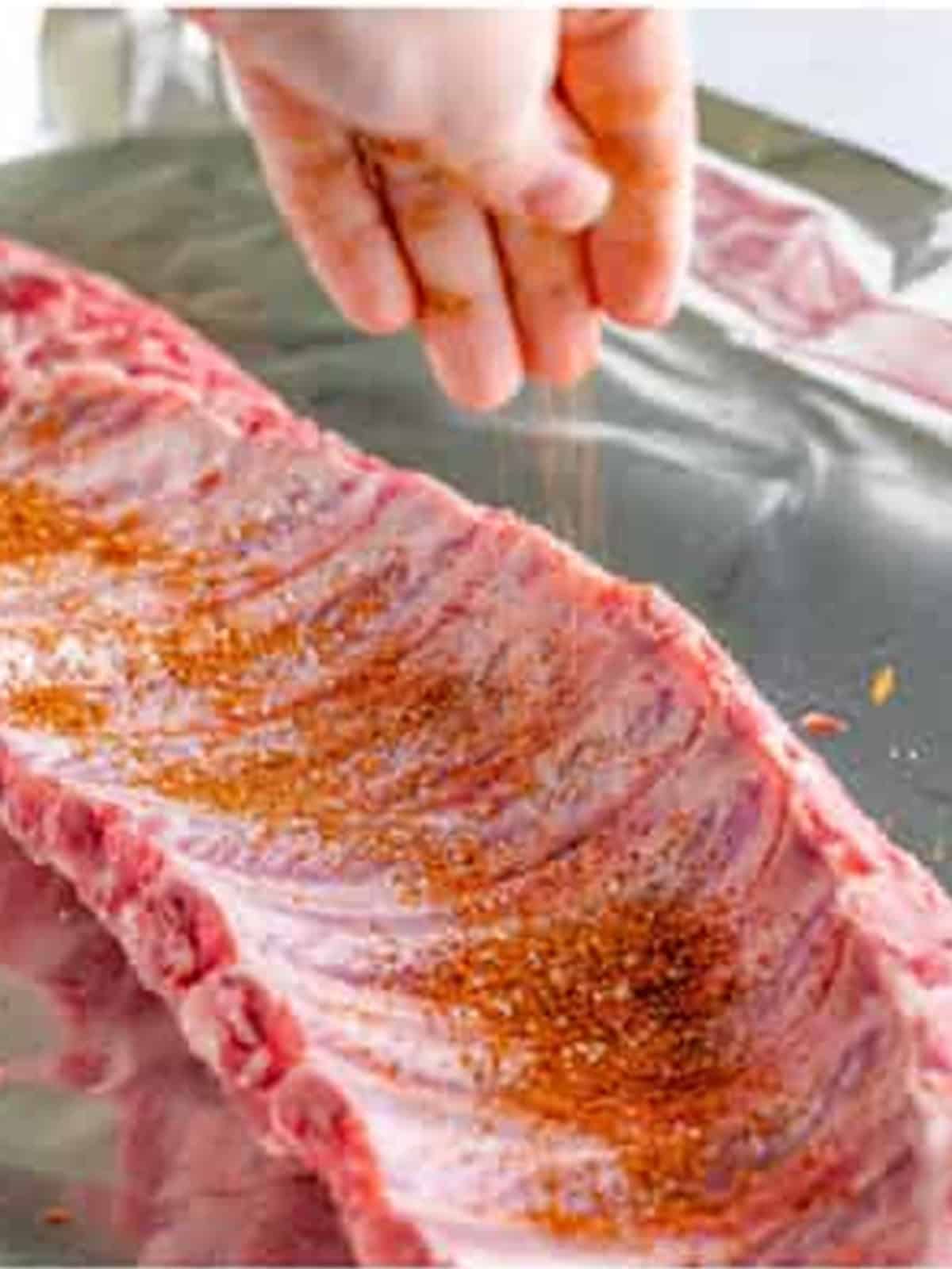 Sprinkling dry rub seasoning all over a rack of ribs.