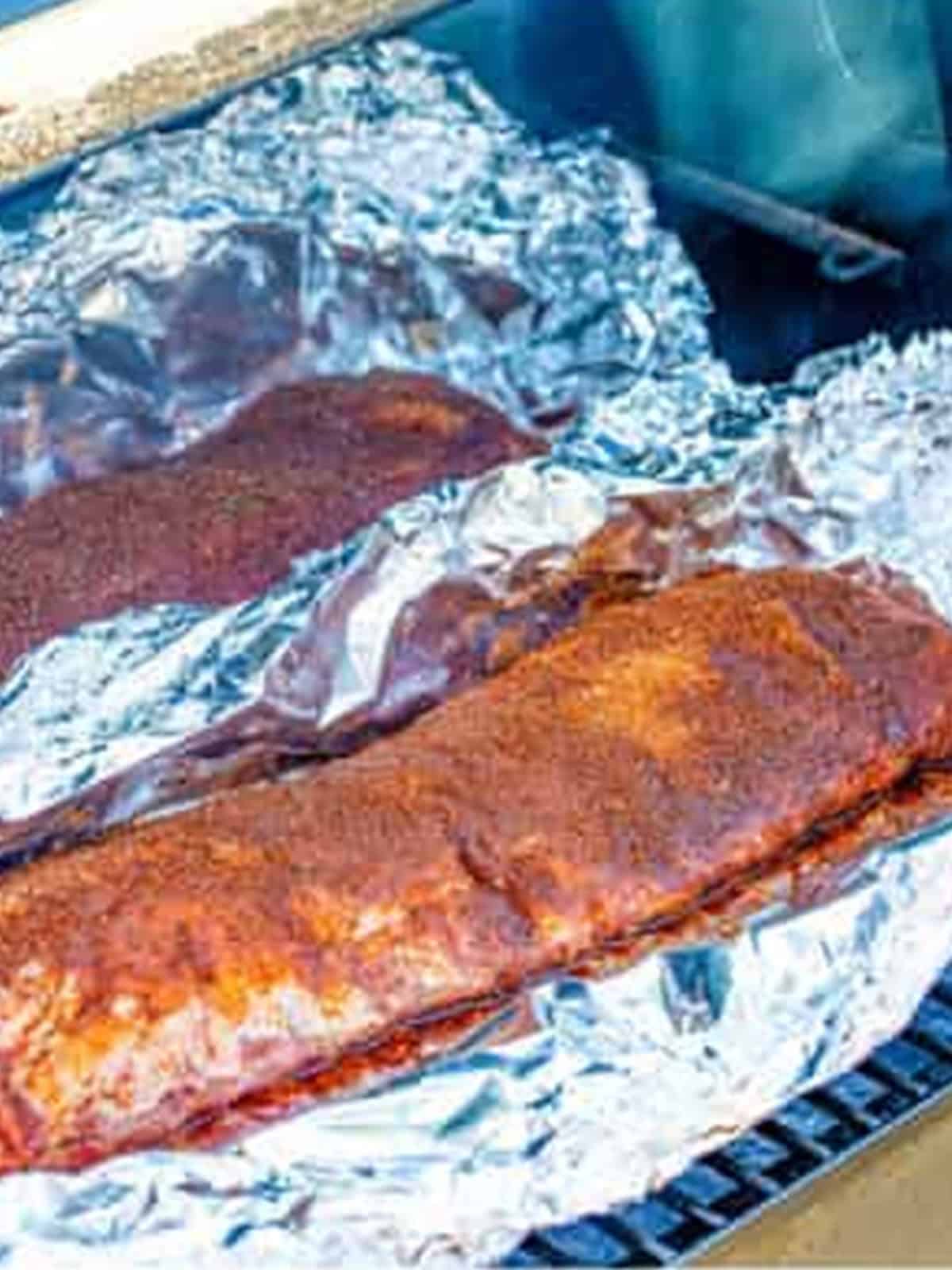 Seasoned ribs on foil smoking low and slow on the grill.