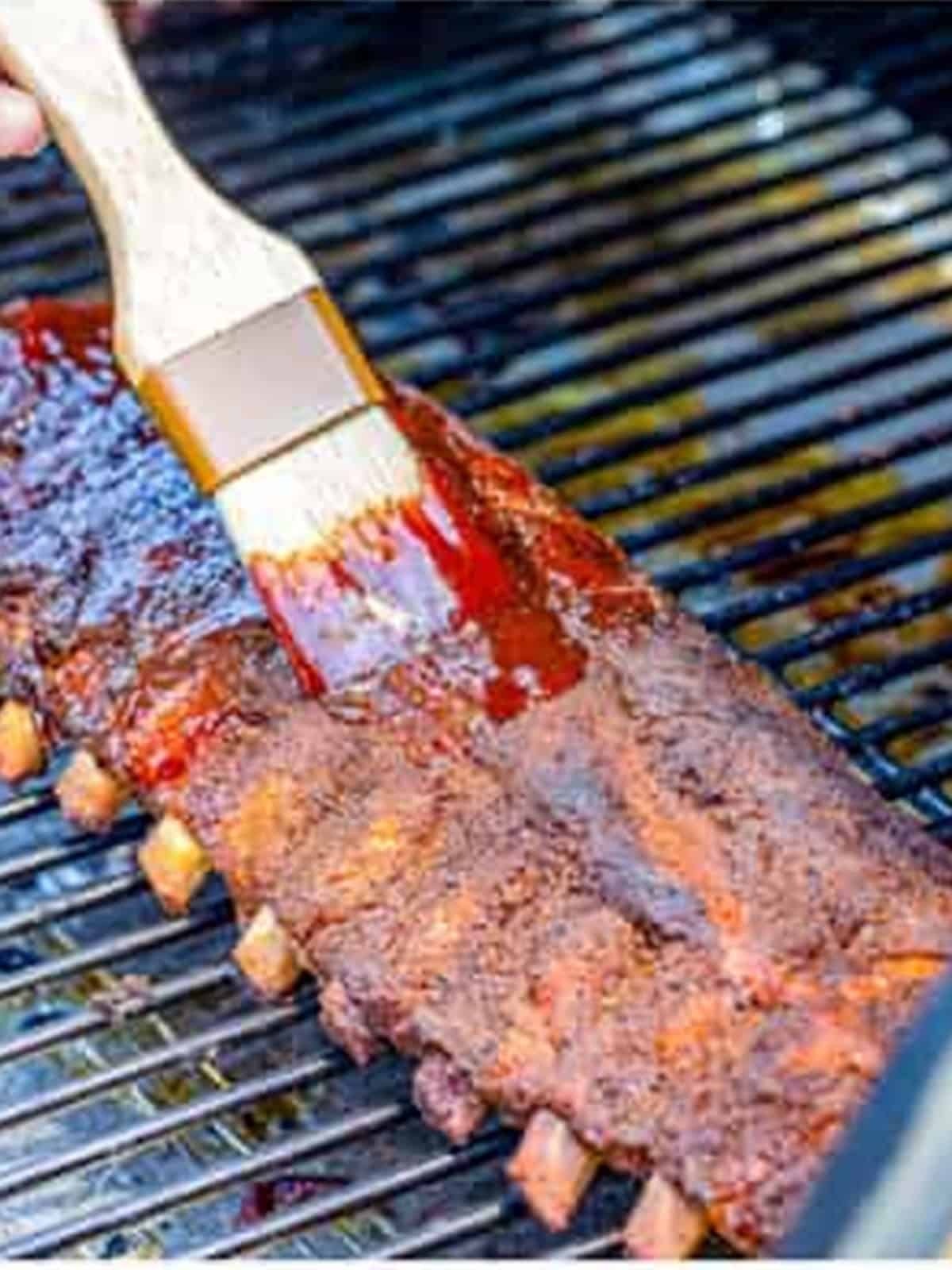 Brushing barbecue sauce onto smoked ribs on the grill.