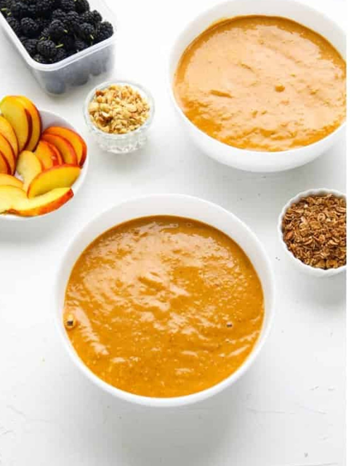 Thick smoothie poured into bowls with toppings set out on the side.