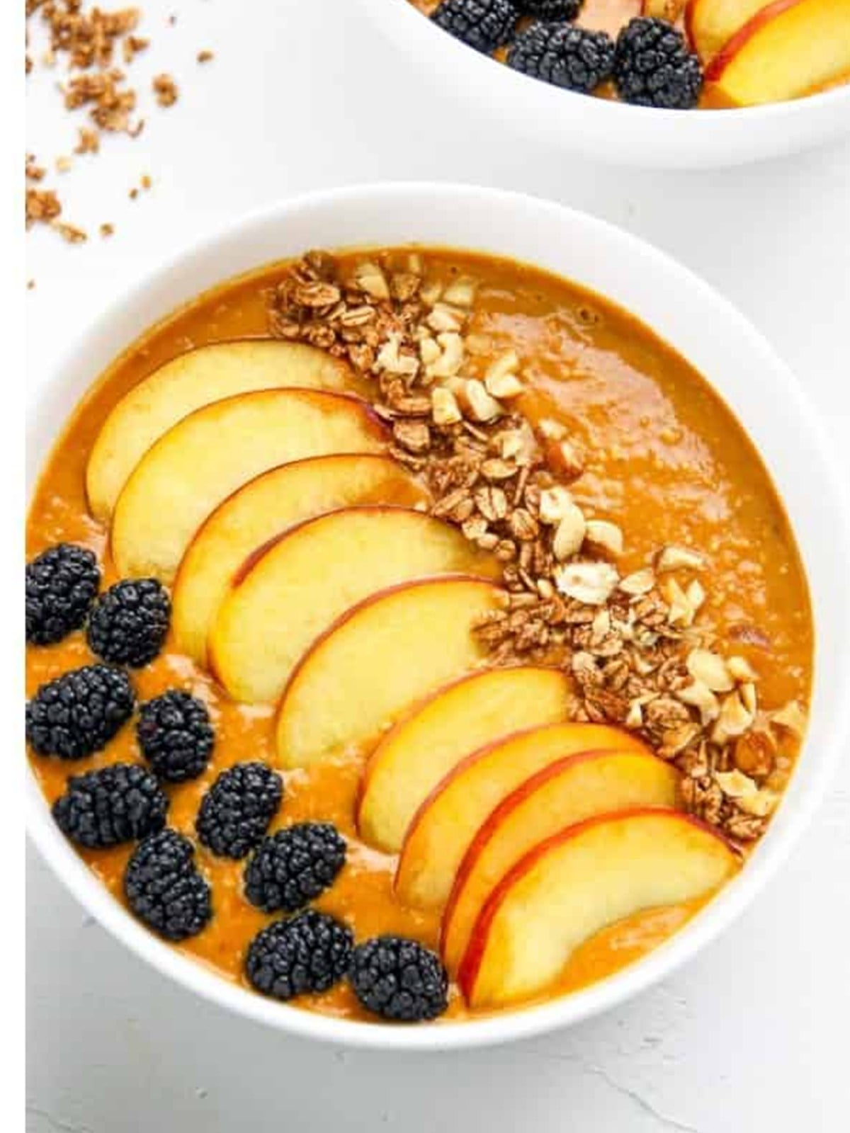 A finished smoothie bowl topped with peach slices, blackberries, granola, and hazelnuts.