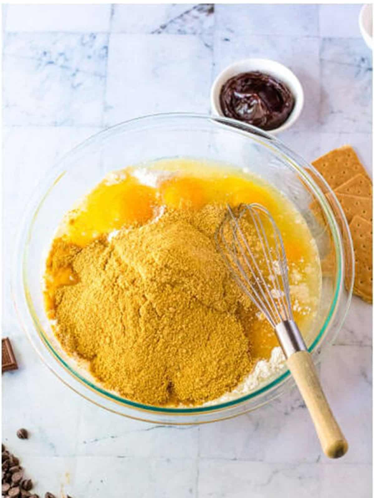 Yellow cake mix, eggs, oil, and graham cracker crumbs whisked together in a glass bowl for s'mores cake.