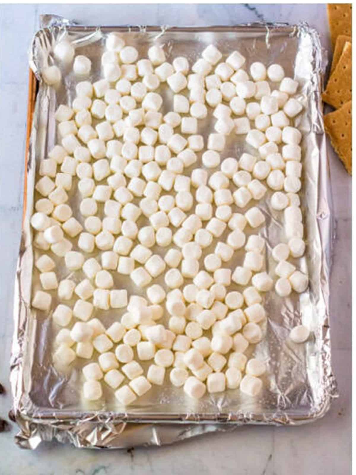 Mini marshmallows spread on a foil lined pan to toast for s'mores cake.