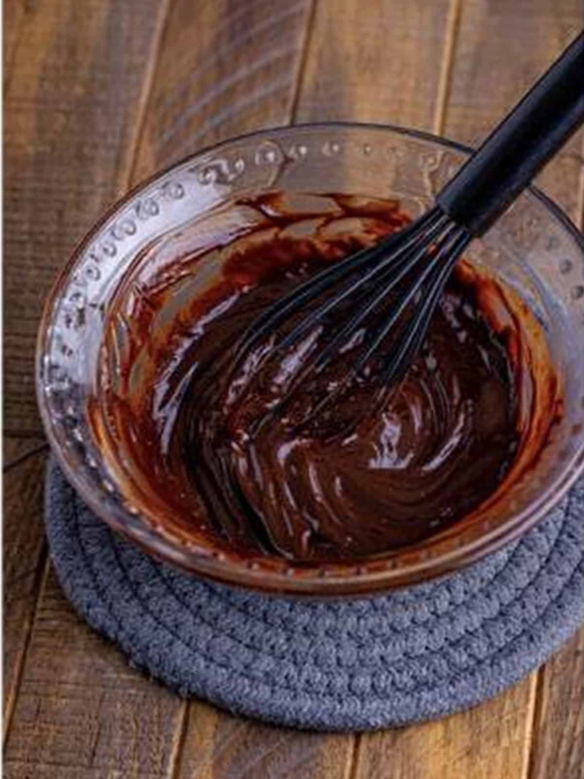 Whisking smooth chocolate ganache in a glass bowl.