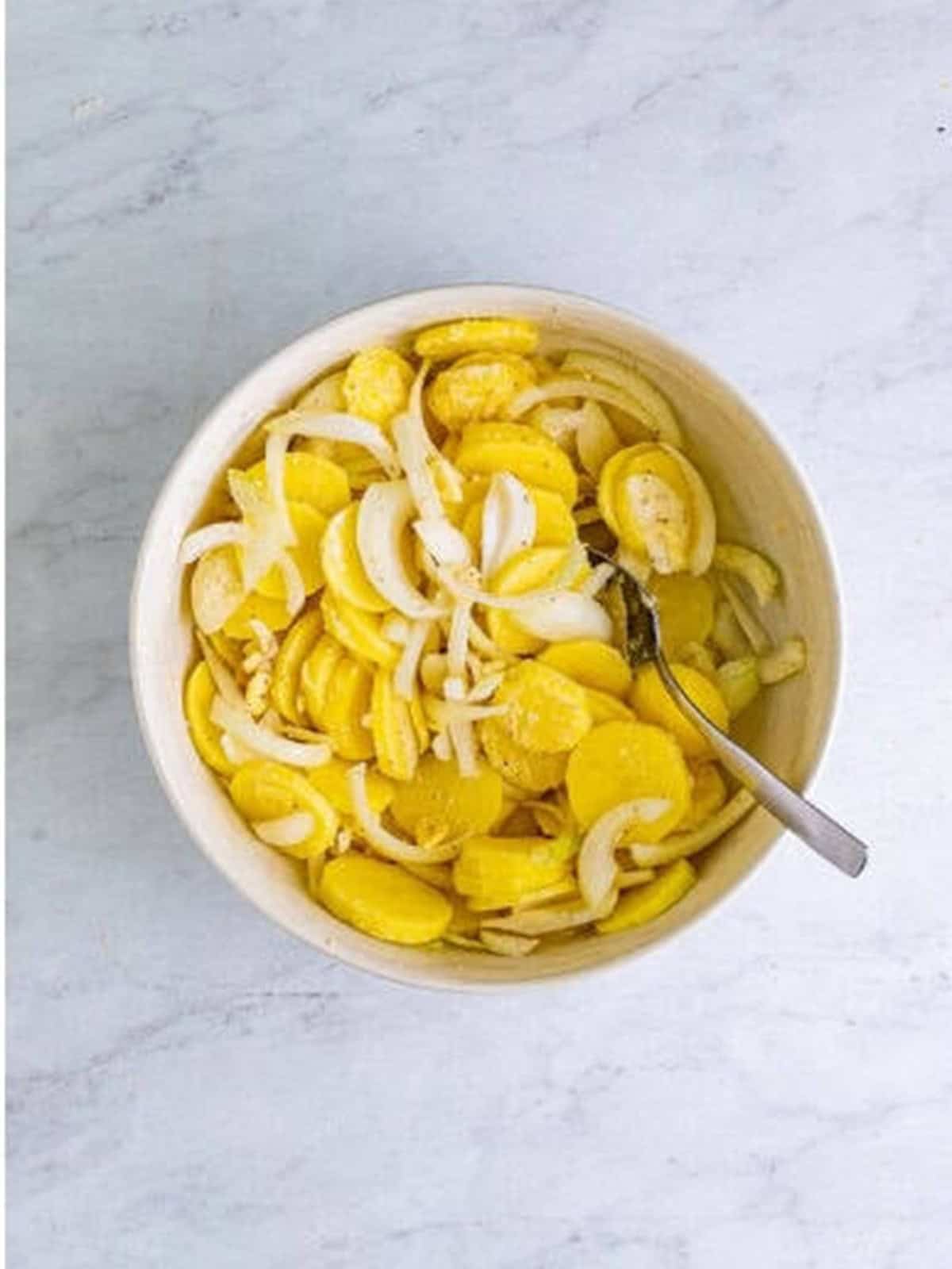Potato and onion mixture stirred together in a large bowl for smothered potatoes.