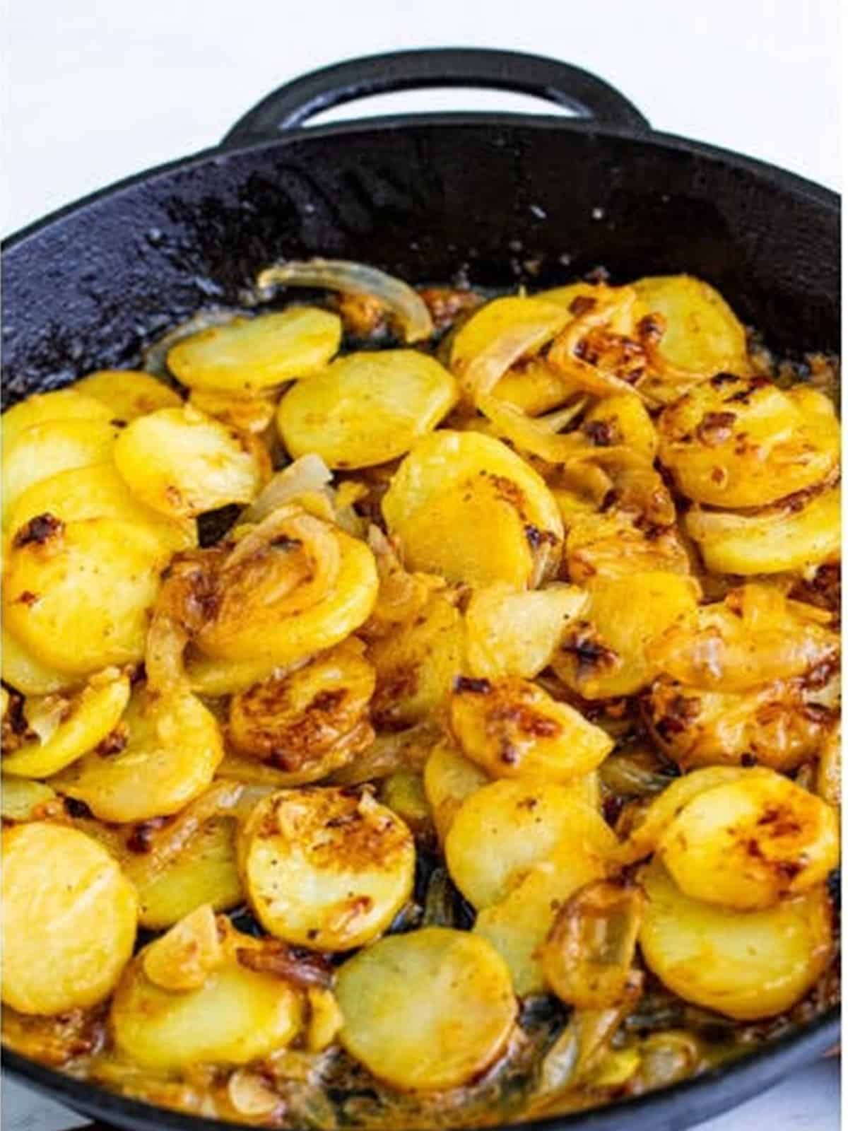 Potatoes and onions browning in a cast iron skillet for smothered potatoes.