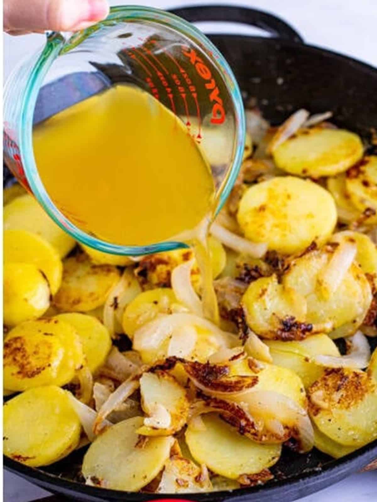 Chicken stock poured over browned potatoes in a cast iron skillet for smothered potatoes.