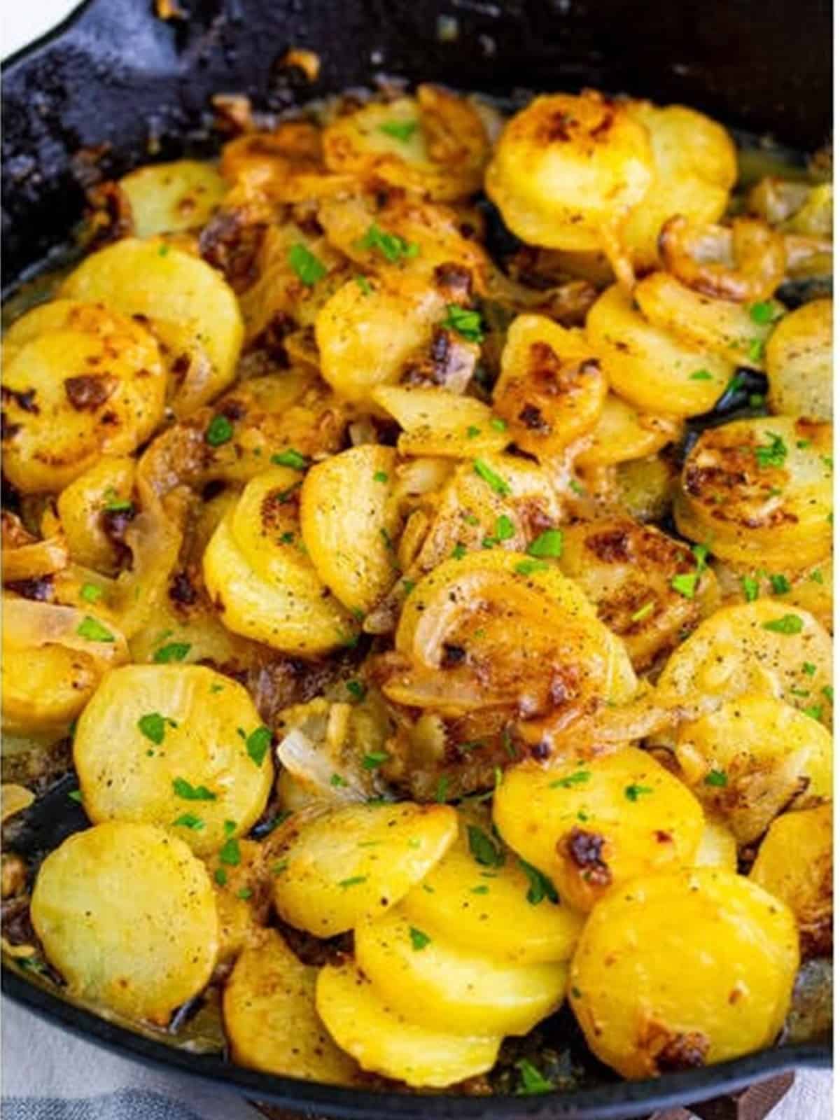 Finished smothered potatoes in a cast iron skillet garnished with fresh parsley.