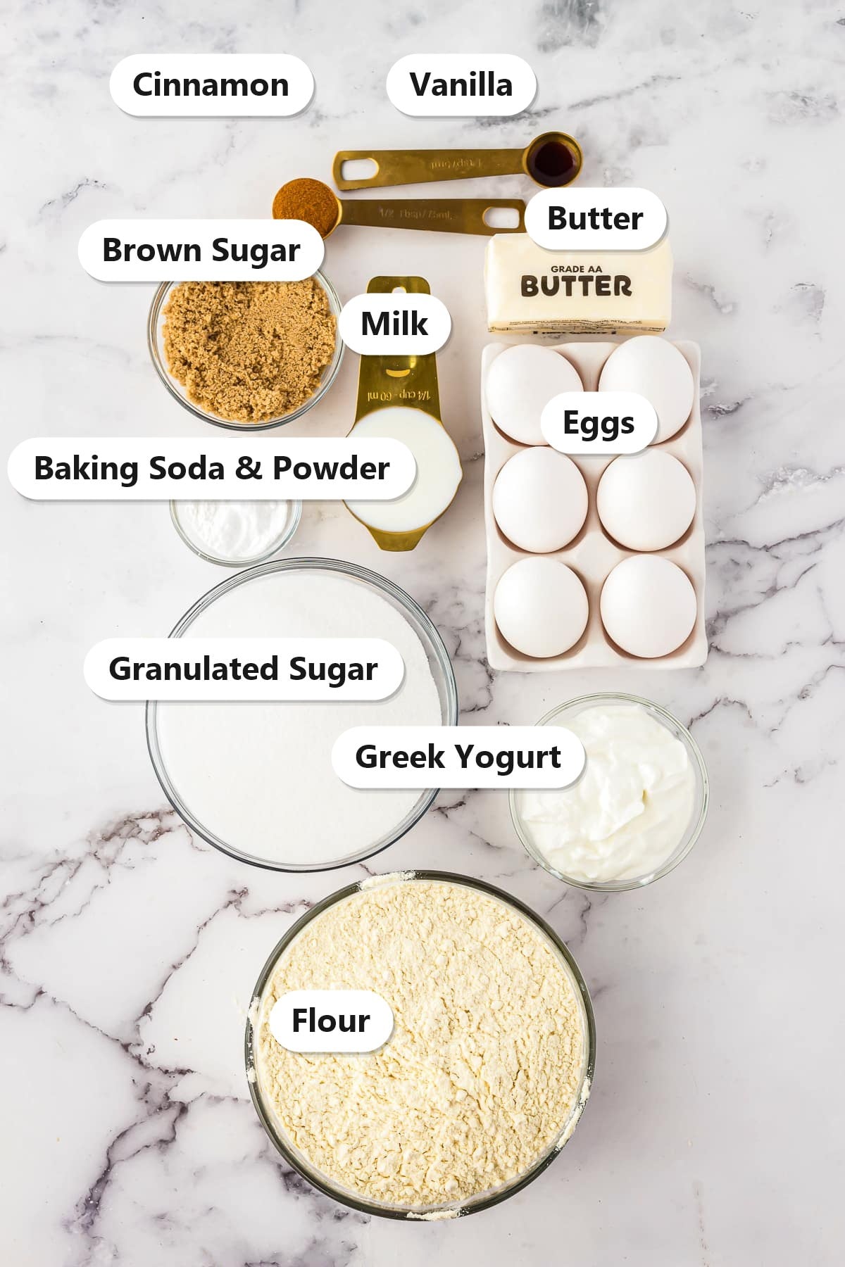 Labeled ingredients for snickerdoodle cake: cinnamon, vanilla, butter, brown sugar, milk, eggs, baking soda and powder, granulated sugar, Greek yogurt, and flour.