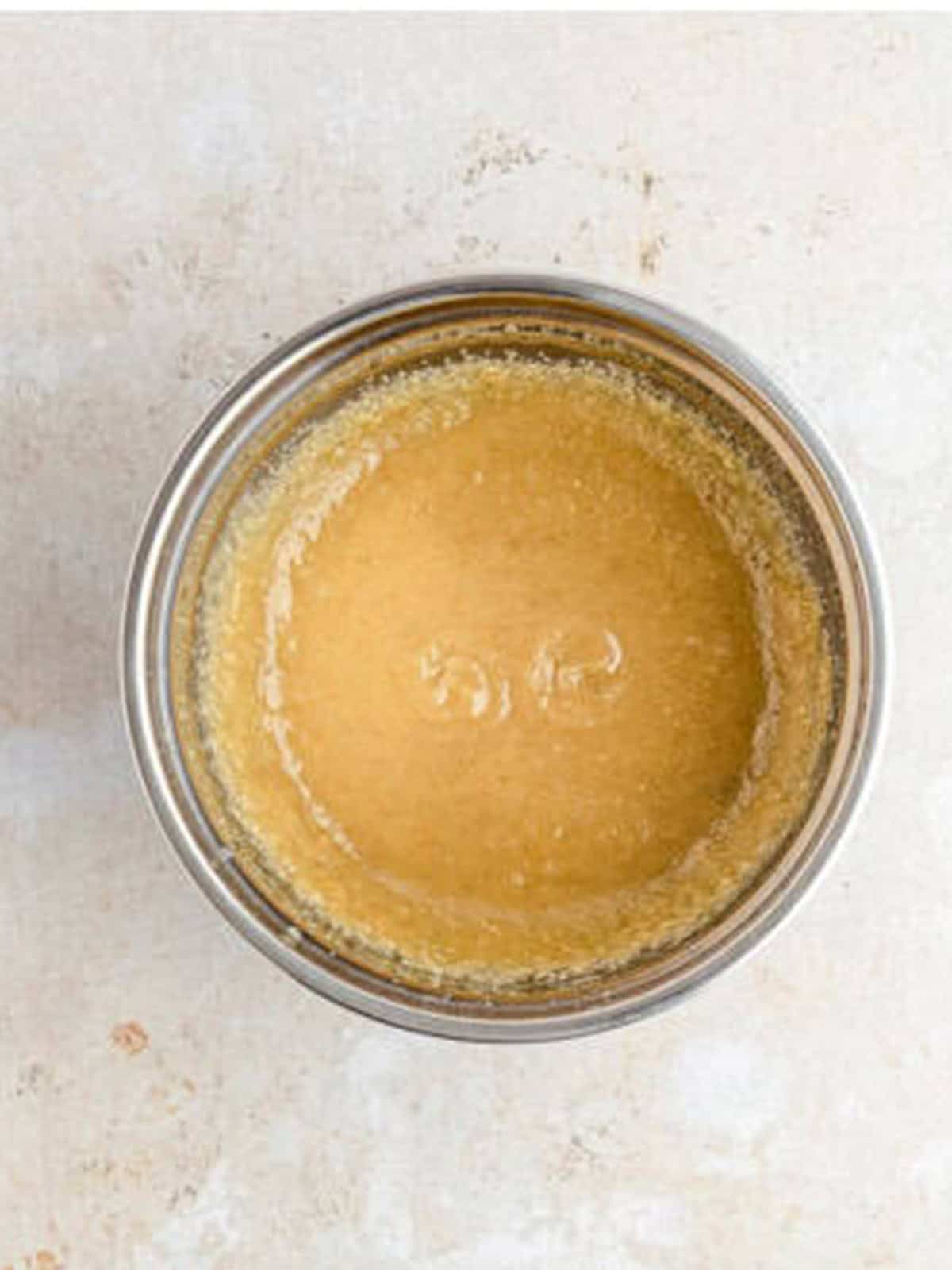 Creaming melted butter with granulated and brown sugar in a glass bowl for snickerdoodle cookies.