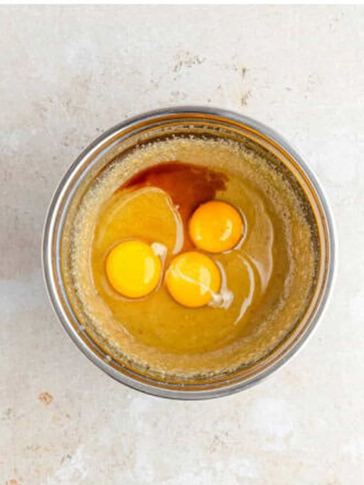 Adding eggs, egg yolk, and vanilla to the creamed butter and sugar mixture.