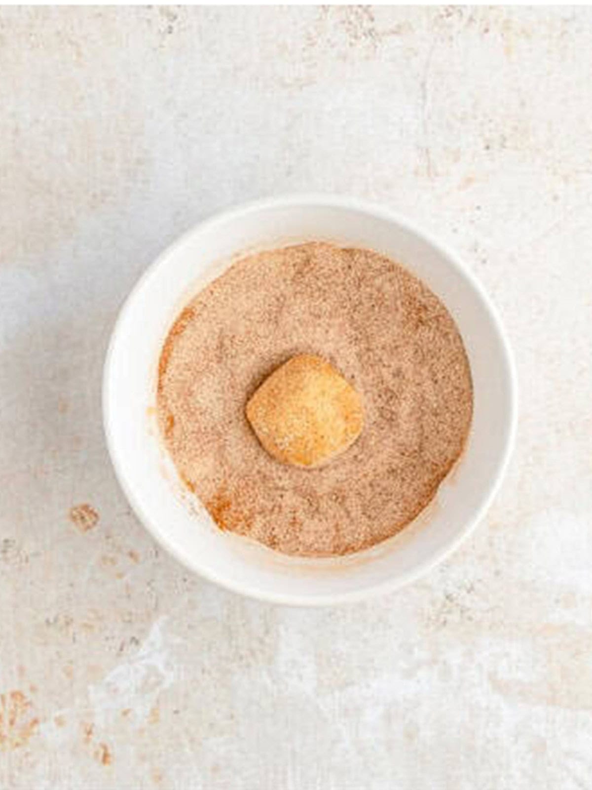 Rolling a snickerdoodle dough ball in a bowl of cinnamon sugar.