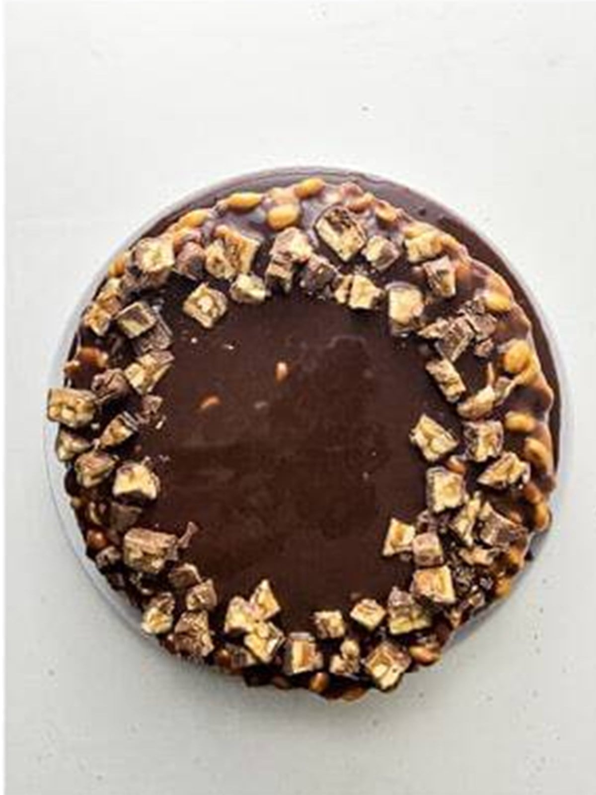 Finished Snickers cheesecake topped with chocolate ganache and Snickers chunks.