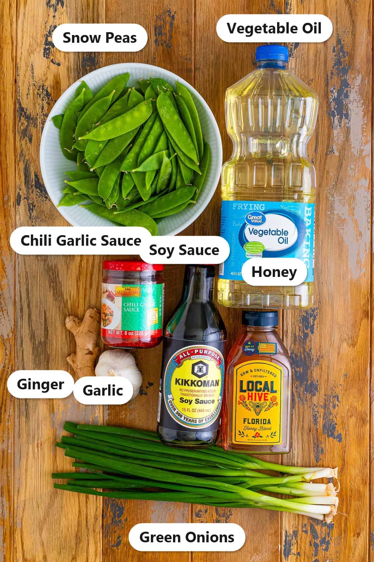 Labeled ingredients needed to make this snow peas recipe including snow peas, vegetable oil, soy sauce, chili garlic sauce, honey, ginger, garlic, and green onions.