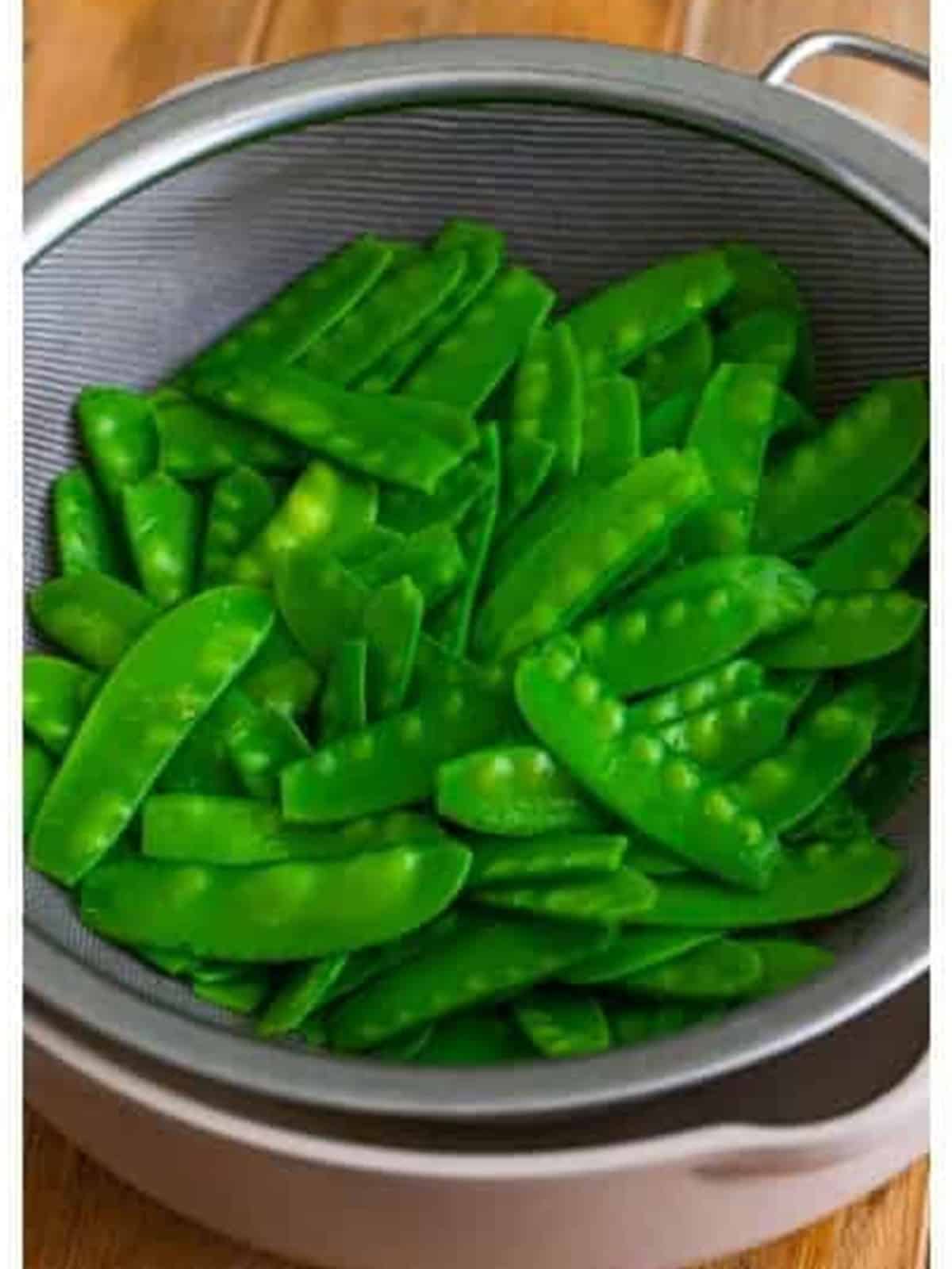 Blanched snow peas draining in a strainer after 30 seconds in boiling water.