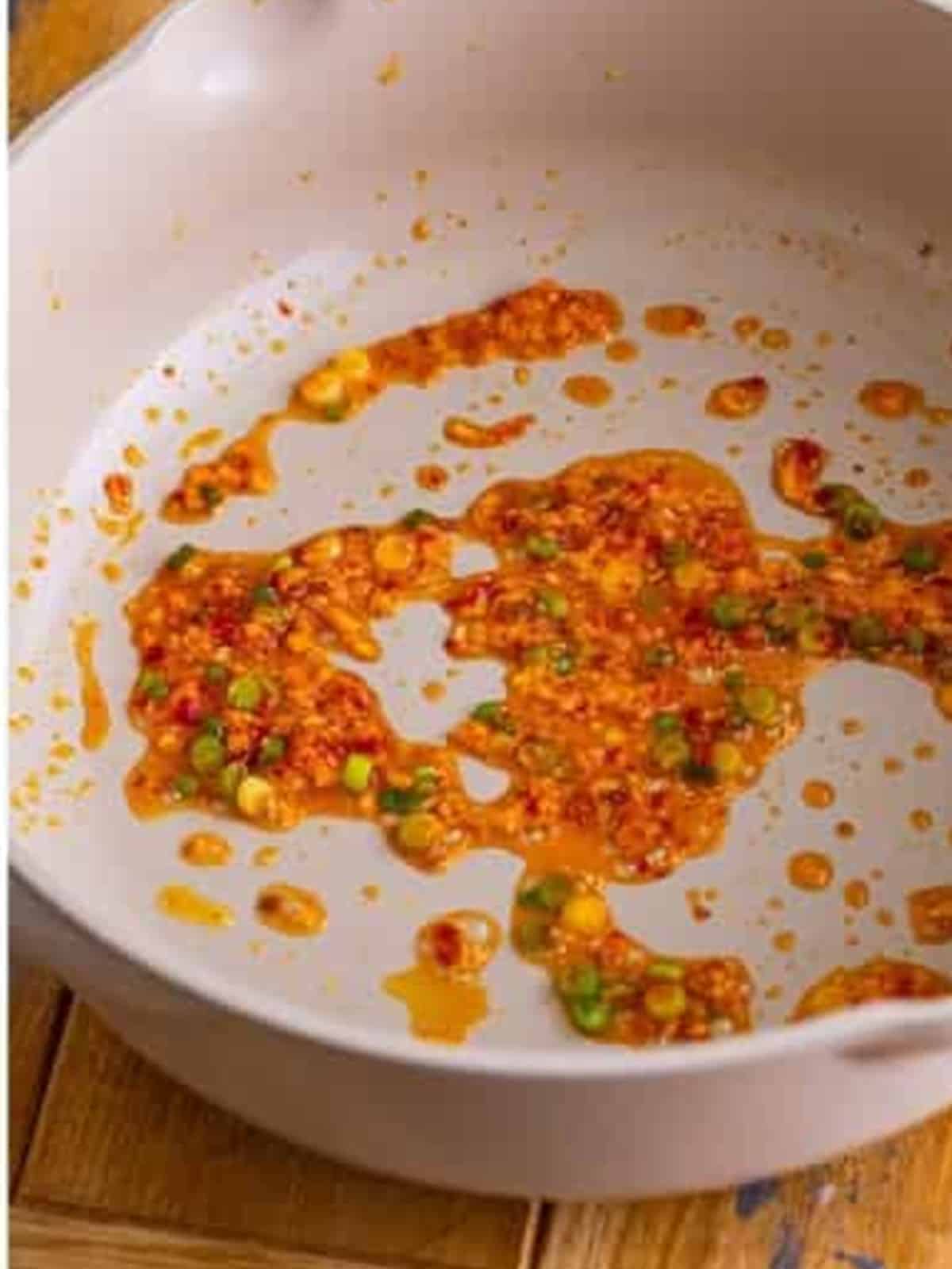 Garlic, ginger, scallions, and chili garlic sauce cooking in a pan until fragrant.