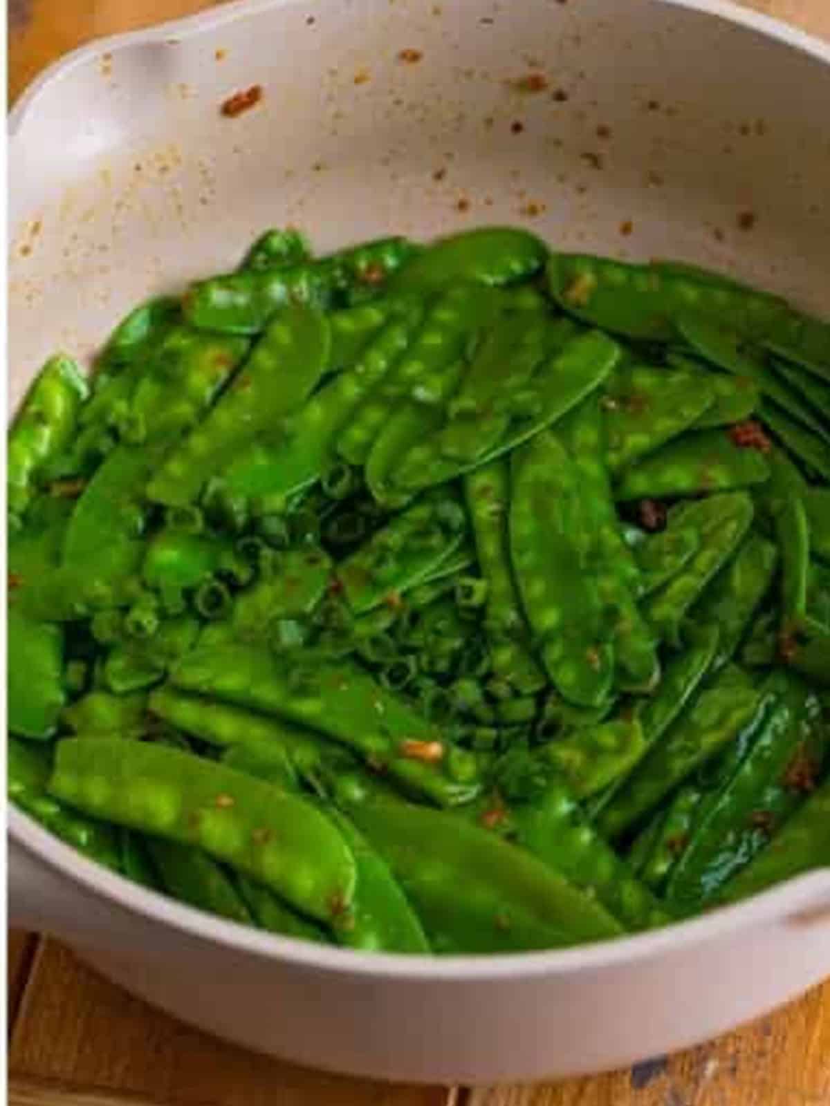 Finished snow peas tossed in garlic ginger sauce with scallion garnish in the pan.