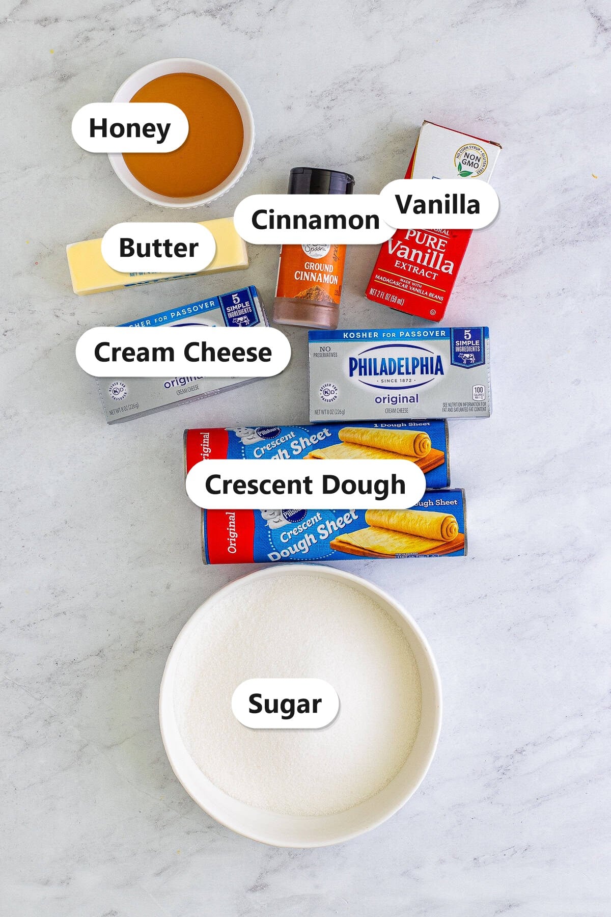 Labeled ingredients to make sopapilla cheesecake including crescent dough, cream cheese, sugar, butter, vanilla, cinnamon, and honey.