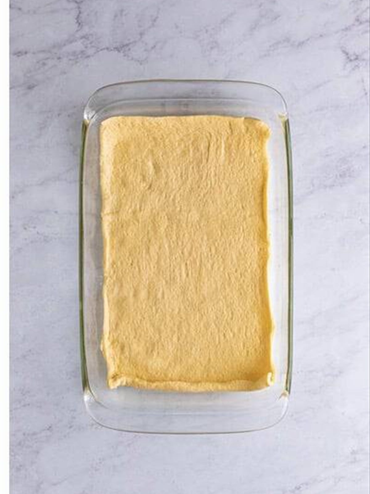 A crescent dough sheet pressed into the bottom of a baking dish for sopapilla cheesecake.