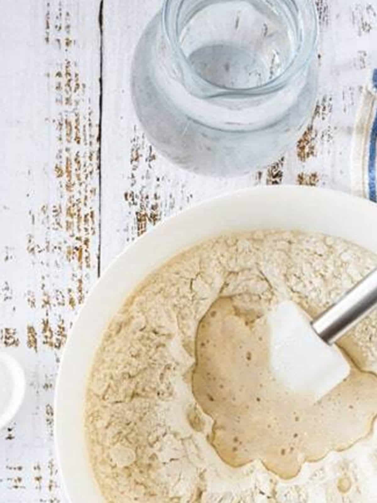 Active sourdough starter added to flour and salt in a bowl for sourdough bread recipe.