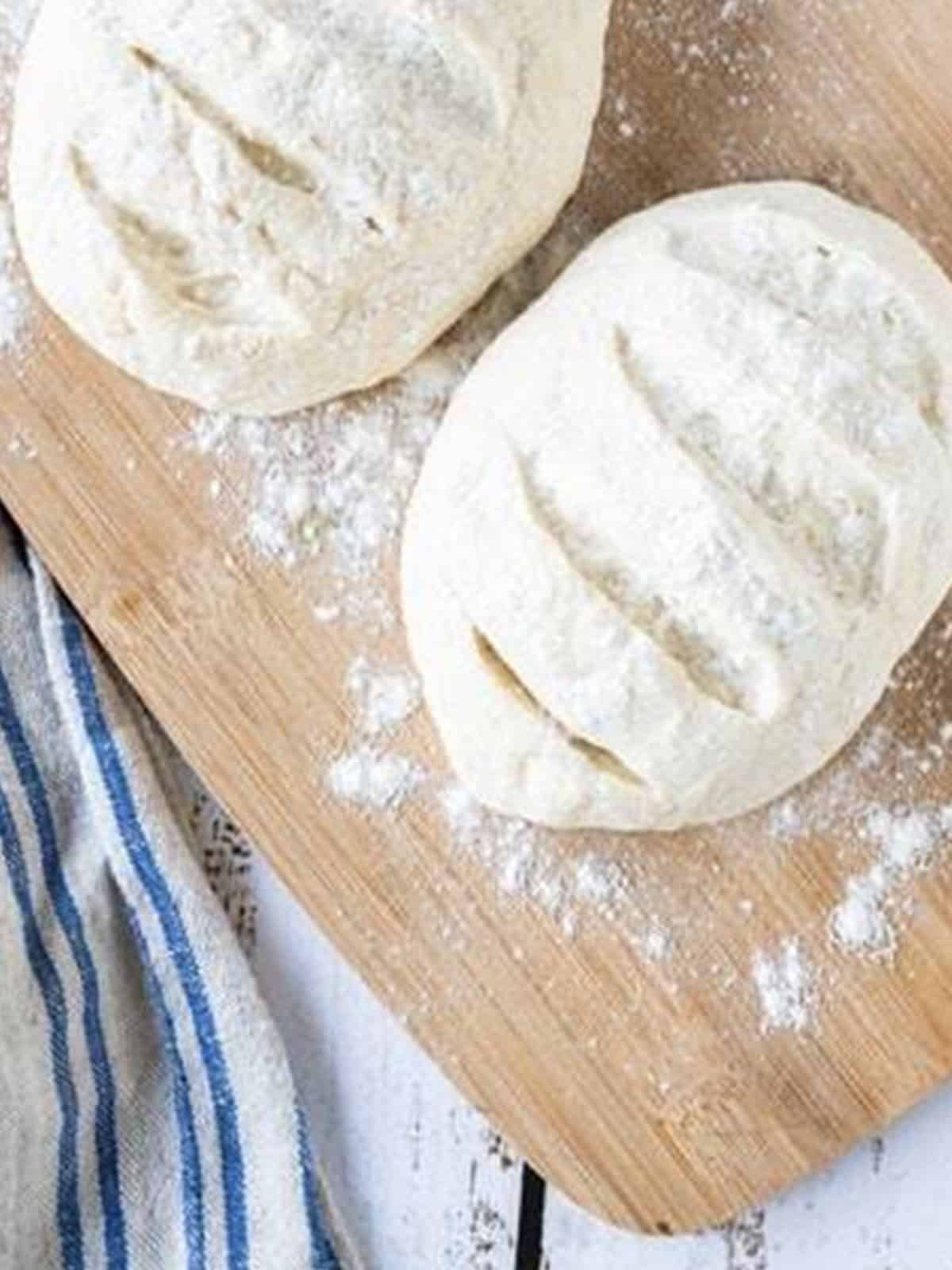 Two shaped and scored sourdough loaves on a floured board for sourdough bread recipe.