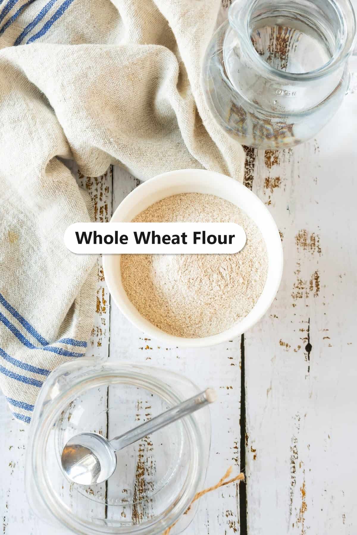 Whole wheat flour in a white bowl with a glass jar, the simple ingredients for a sourdough starter.