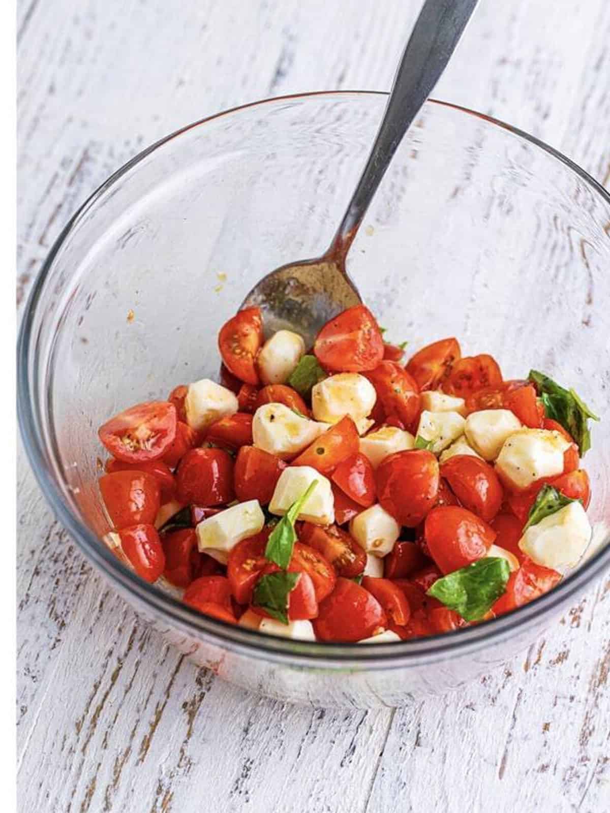 Caprese topping of tomatoes, mozzarella, and basil tossed together in a glass bowl.