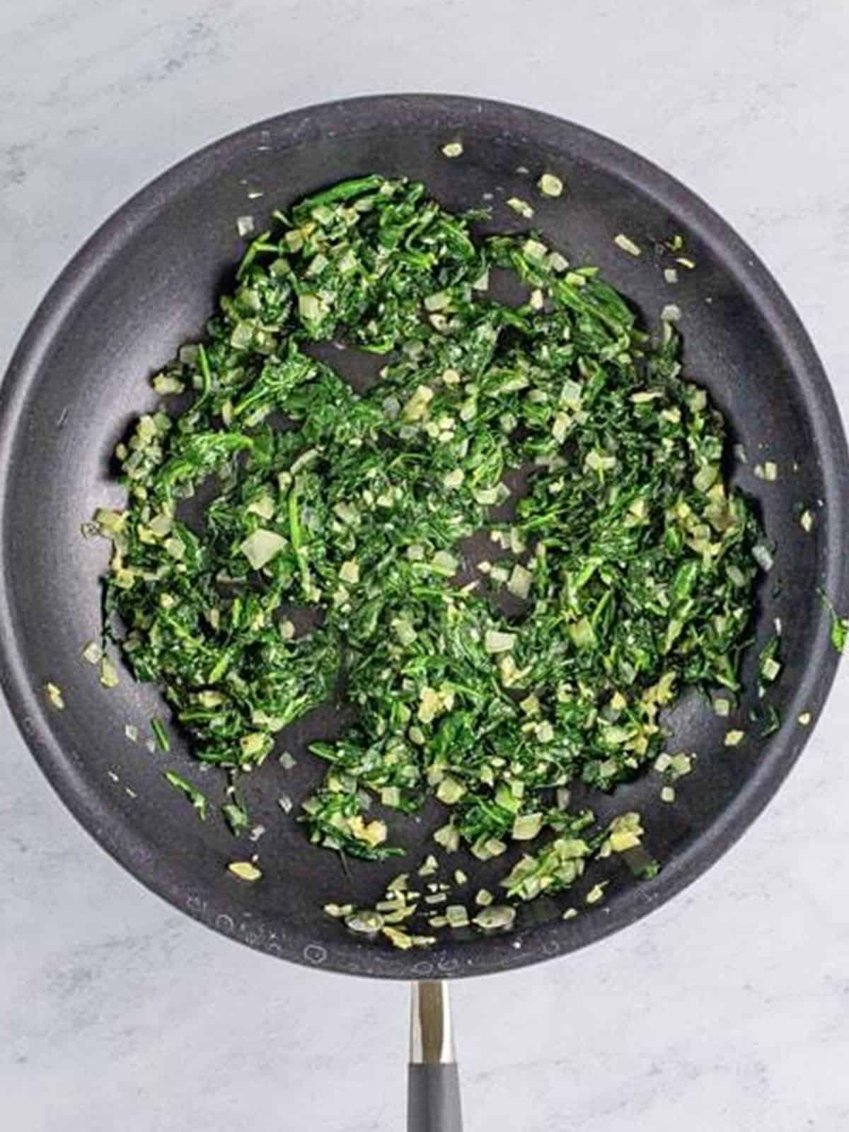 Chopped spinach wilting in the skillet for the spanakopita filling.