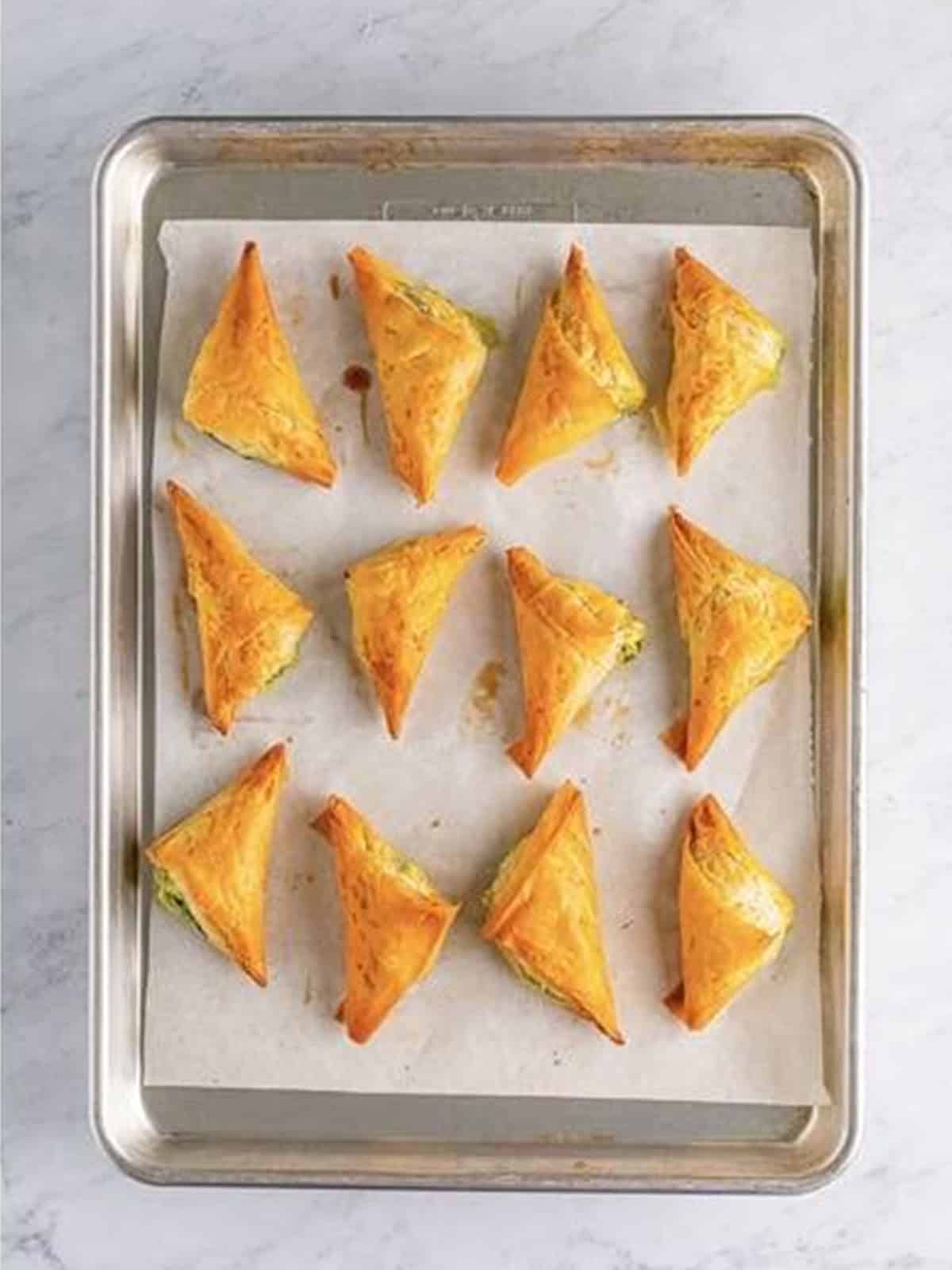Golden baked spanakopita triangles on a sheet pan.