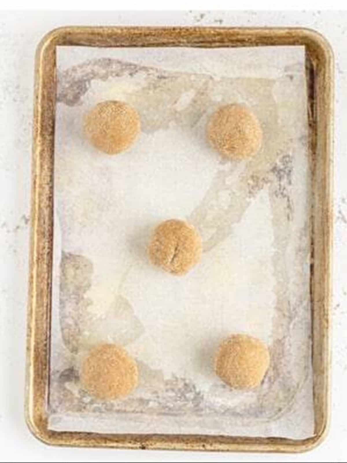 Spice cookie dough balls rolled in cinnamon sugar on a baking sheet.
