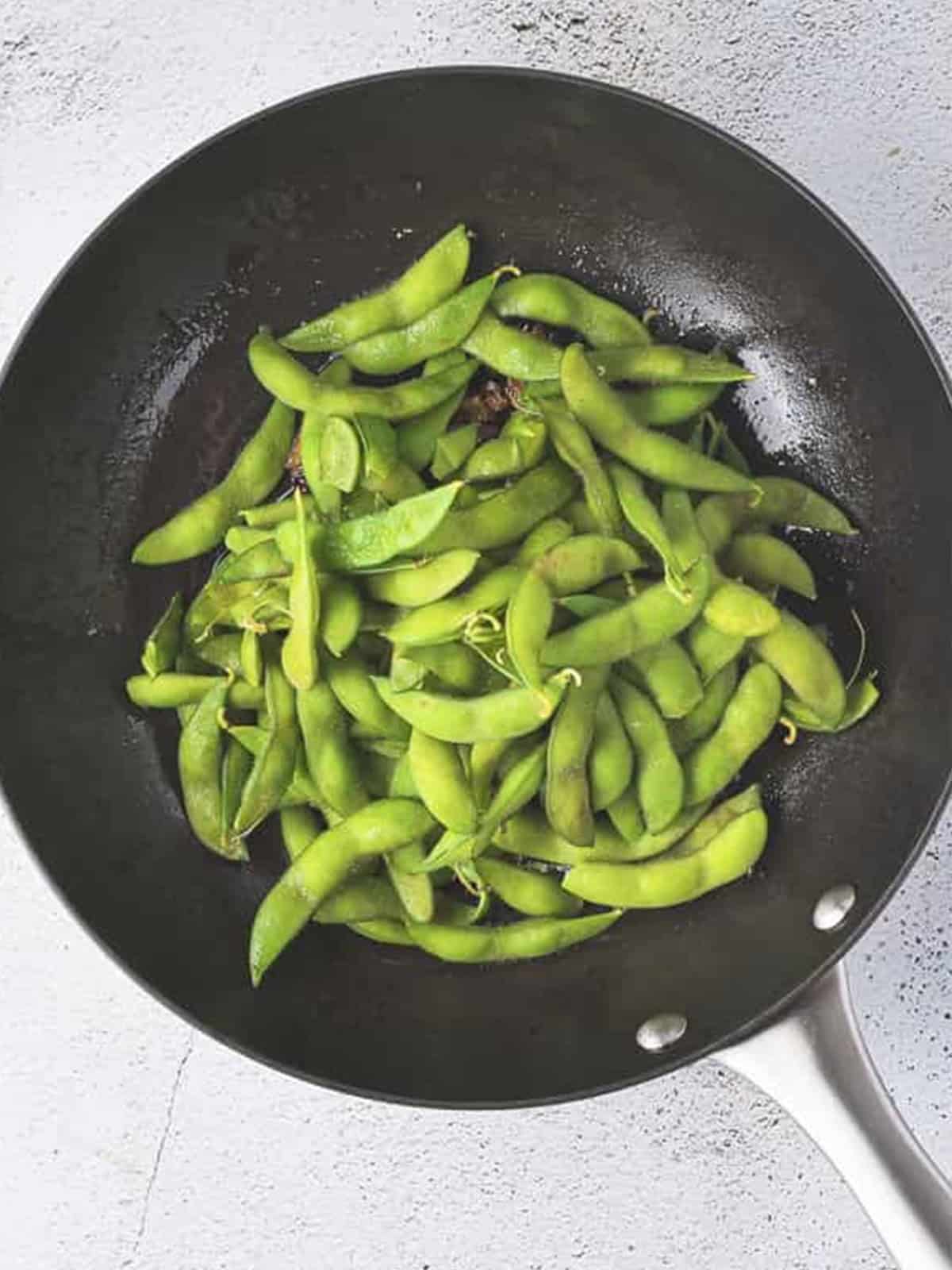 Adding the cooked edamame to the skillet of aromatics.
