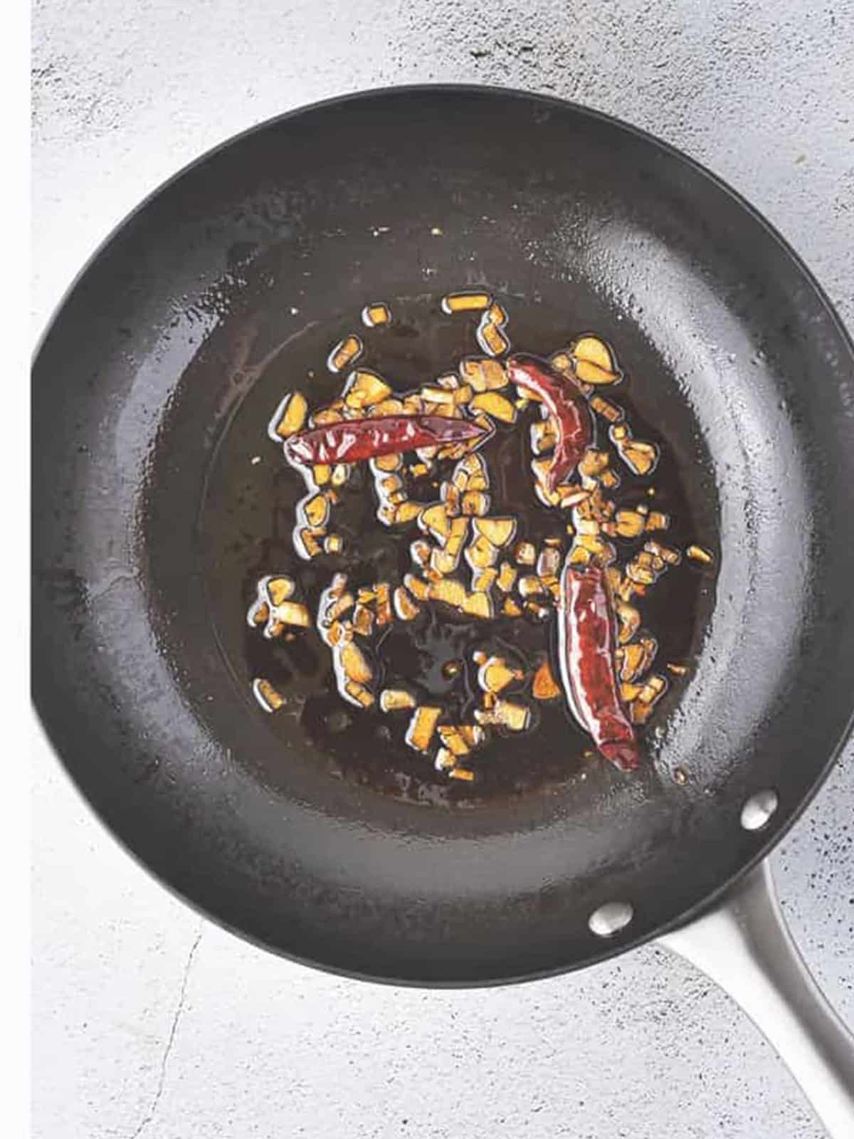 Garlic, dry red chilies, and soy sauce sauteing in a skillet for the edamame recipe.