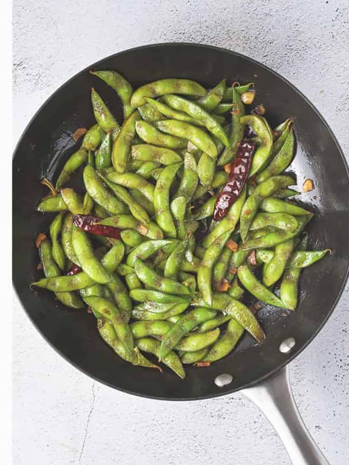 Tossing the spicy garlic edamame in the sauce until coated.