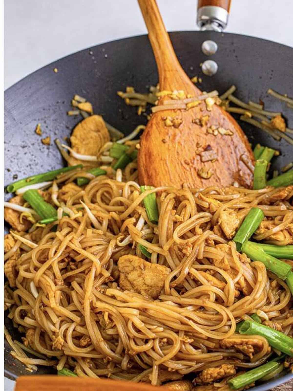 Finished spicy pad thai tossed together in the wok with a wooden spoon.