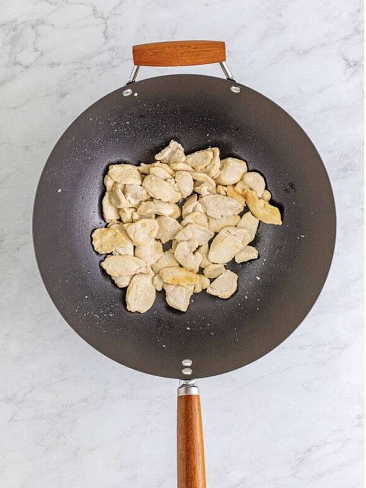 Thinly sliced chicken breast cooked in a hot wok for spicy pad thai recipe.