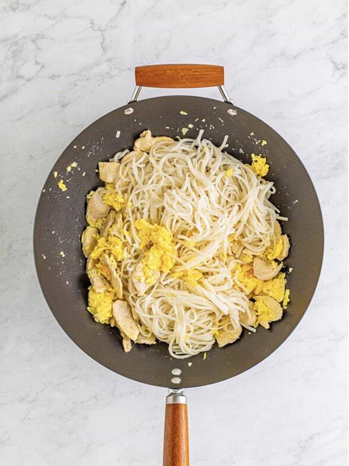 Drained rice noodles added to the wok with the chicken and eggs.