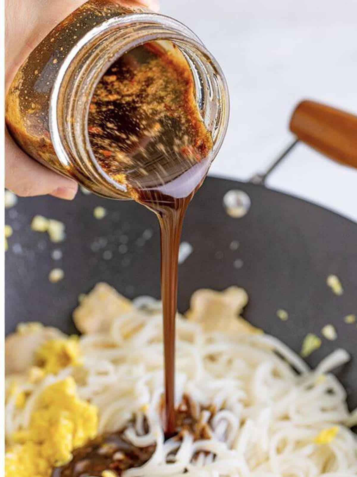 Spicy tamarind pad thai sauce poured from the jar over the noodles in the wok.