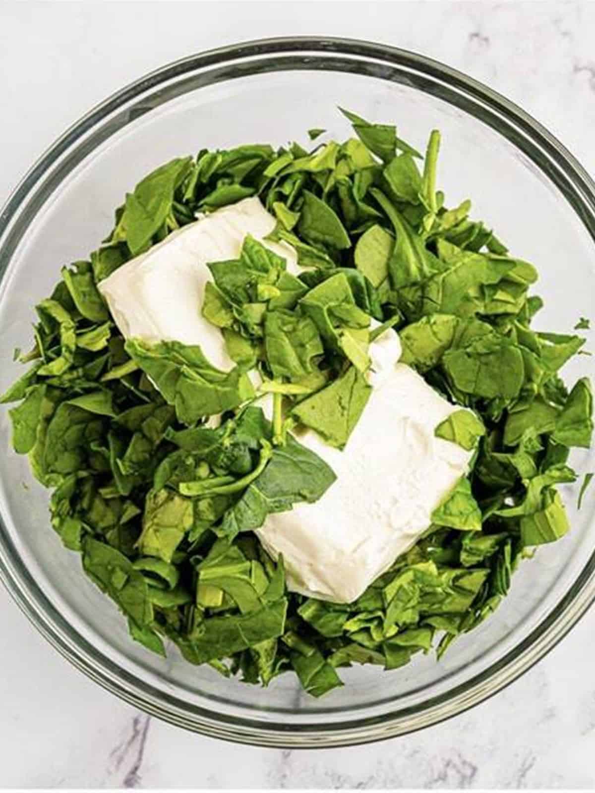 Softened cream cheese and chopped fresh spinach in a glass bowl.