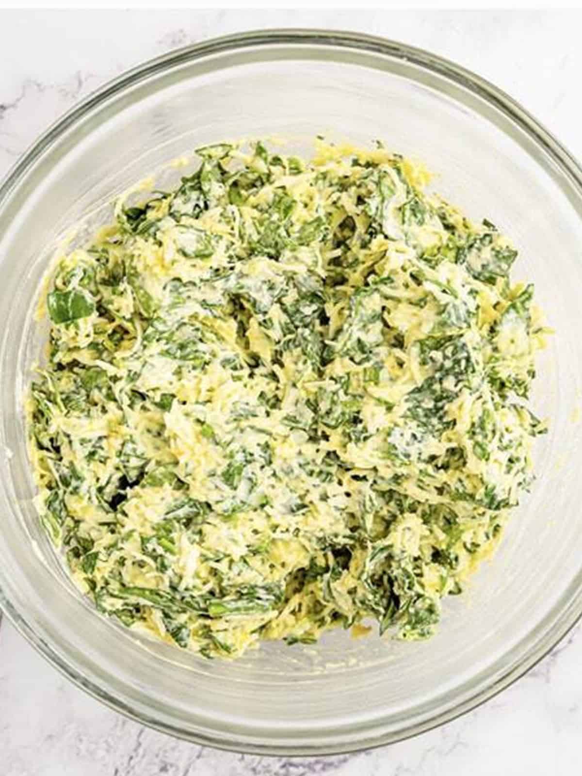 Cheesy spinach filling mixed together in a glass bowl.