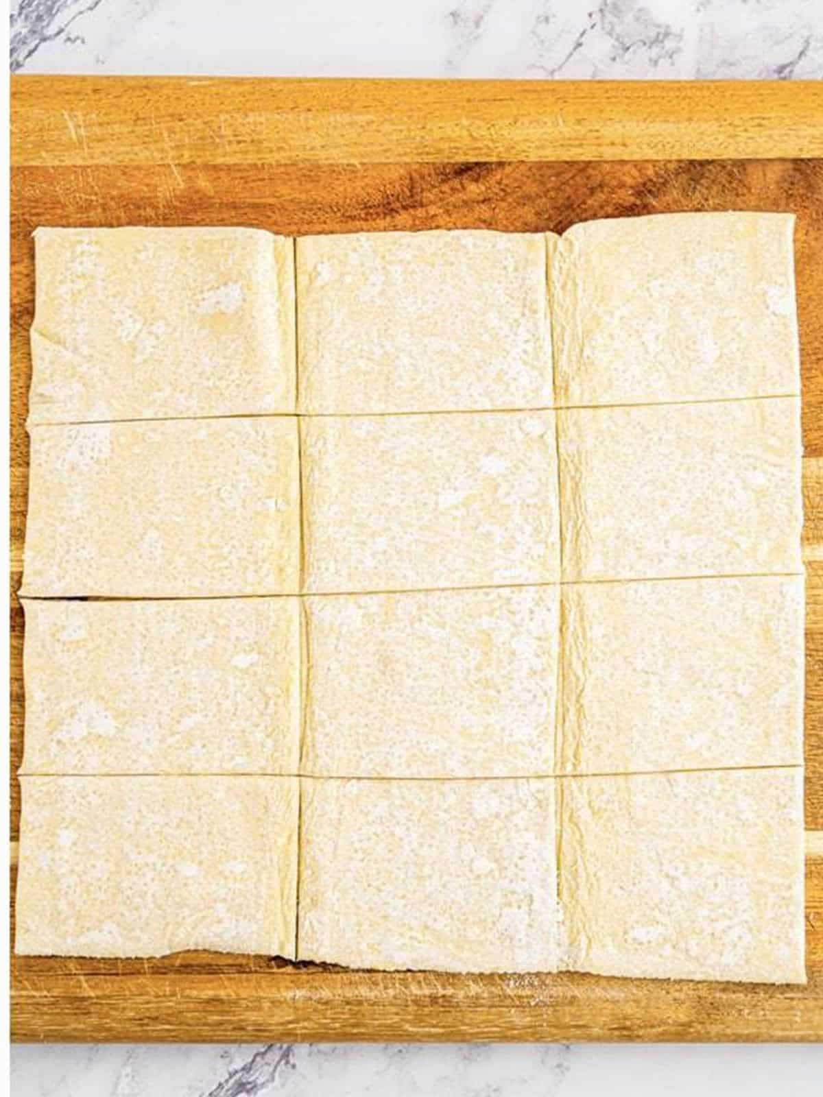 Puff pastry sheet cut into twelve even squares on a cutting board.