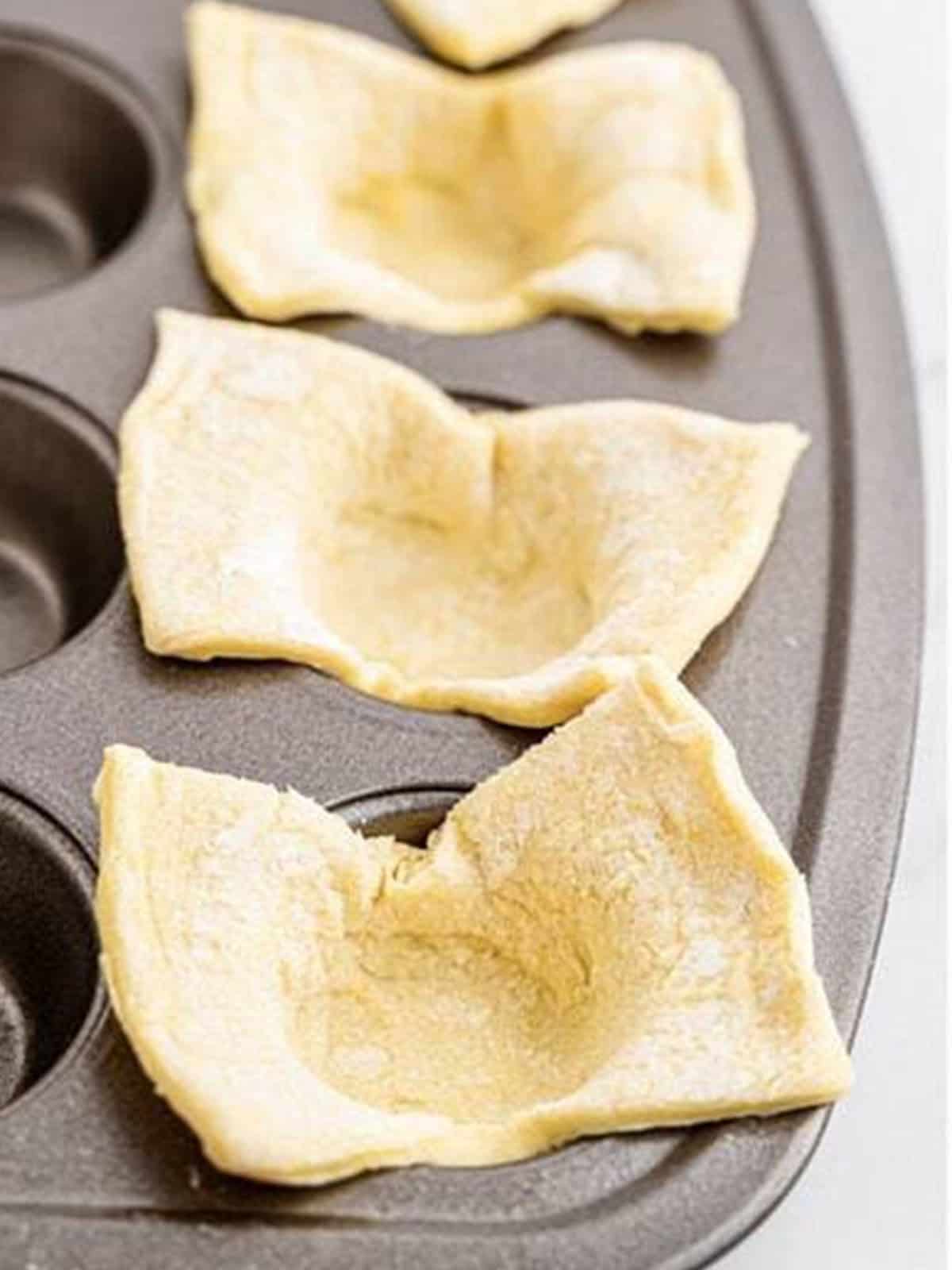 Puff pastry squares pressed into the cavities of a mini muffin tin.
