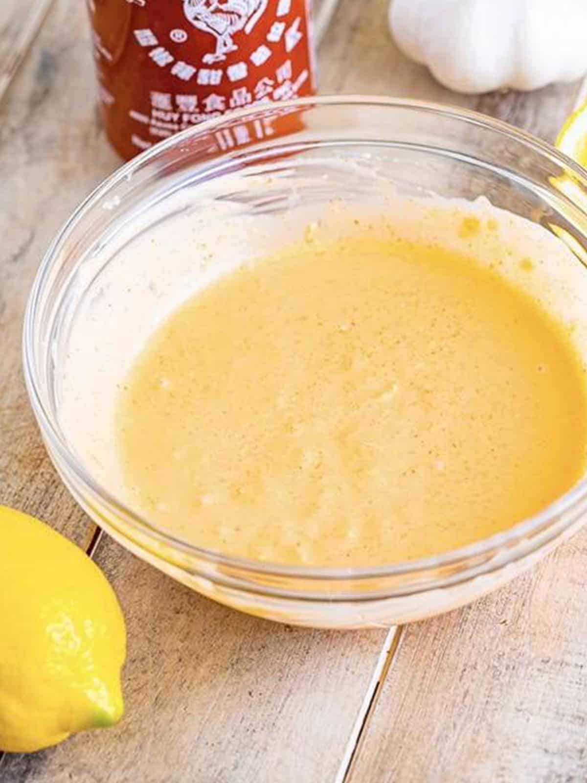Smooth, creamy orange sriracha mayo whisked together in a glass bowl.