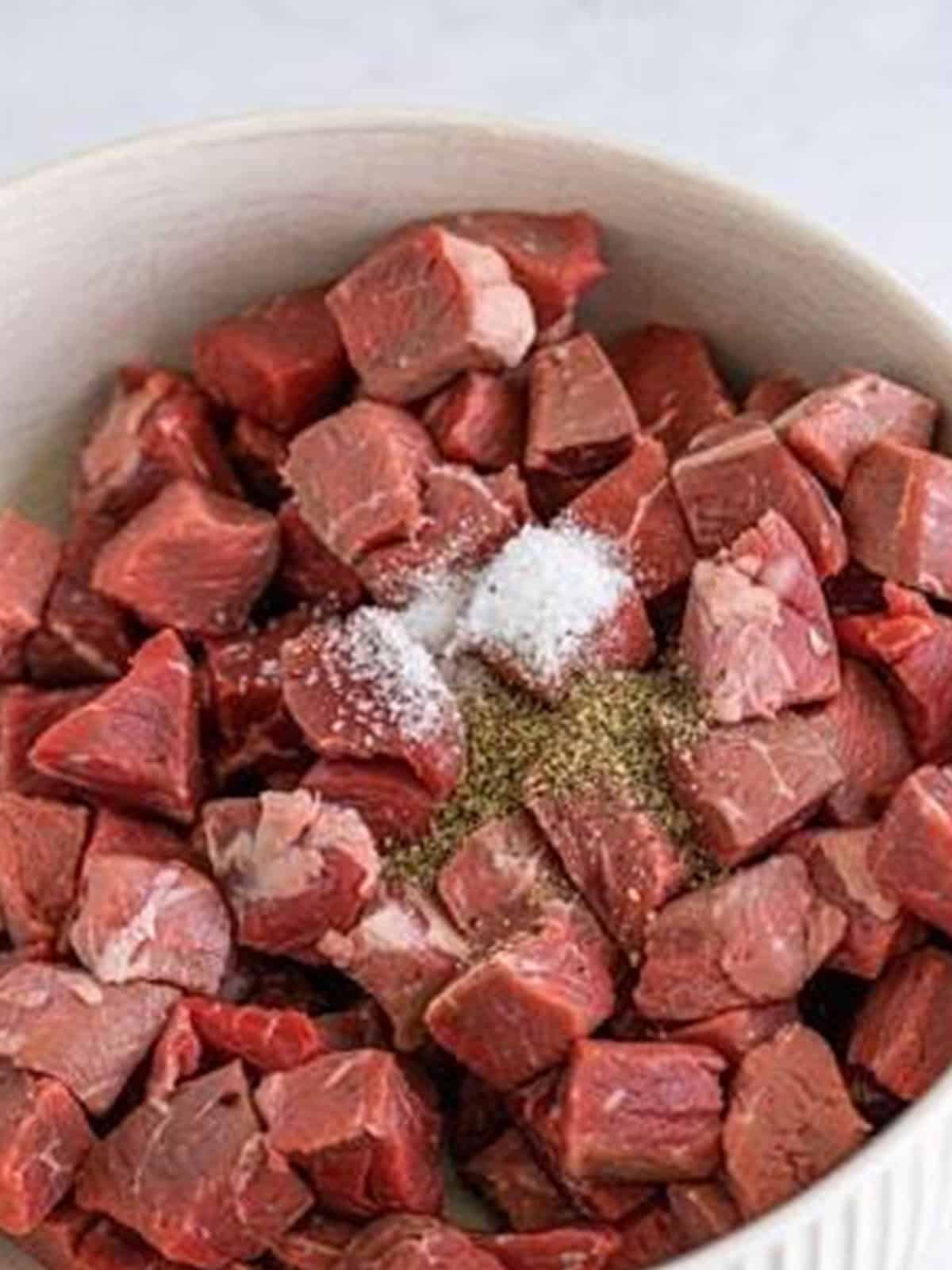Cubed sirloin steak seasoned with salt and pepper in a bowl.