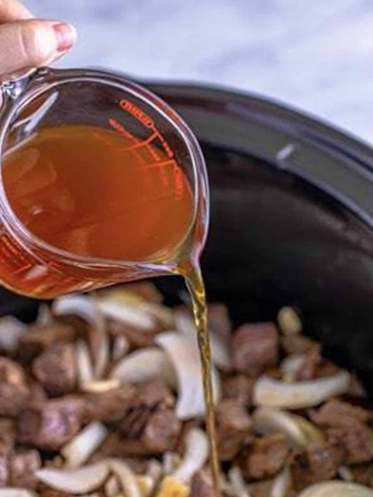 Beef stock being poured over the steak bites in the slow cooker.