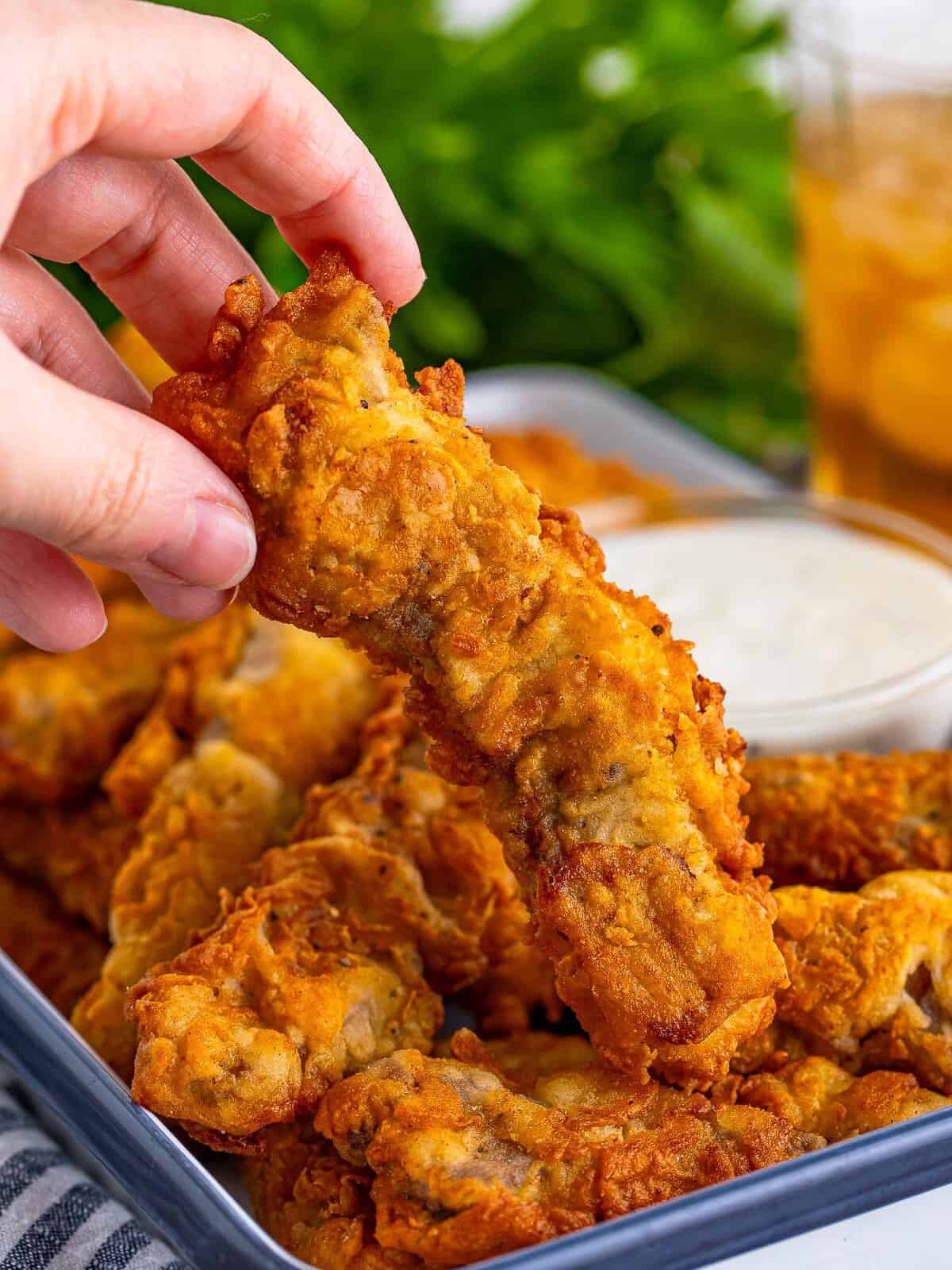 A crispy fried steak finger held over a tray of more steak fingers.