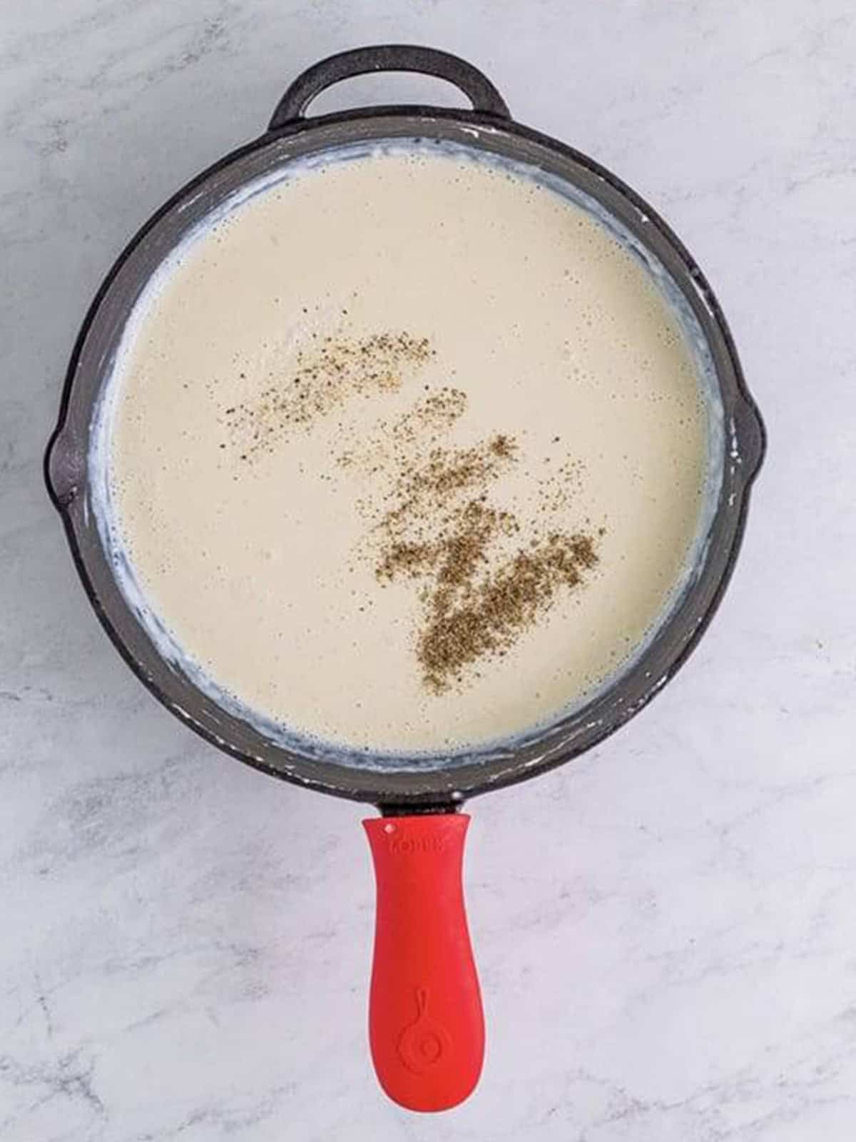 Salt and black pepper added to the gravy in a cast iron skillet.